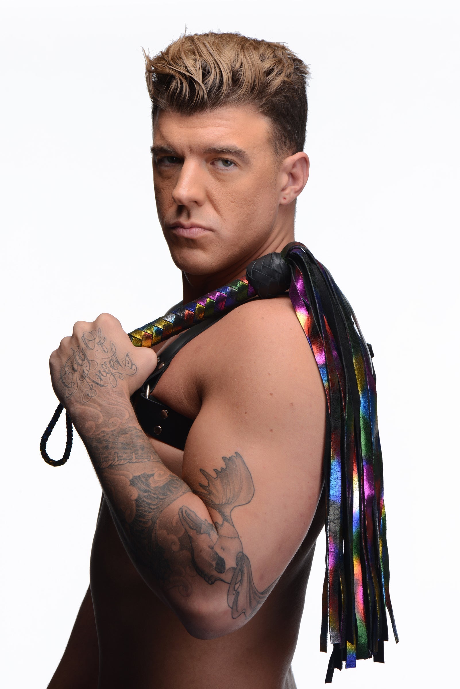 A tattooed individual holding a rainbow leather flogger with a black handle