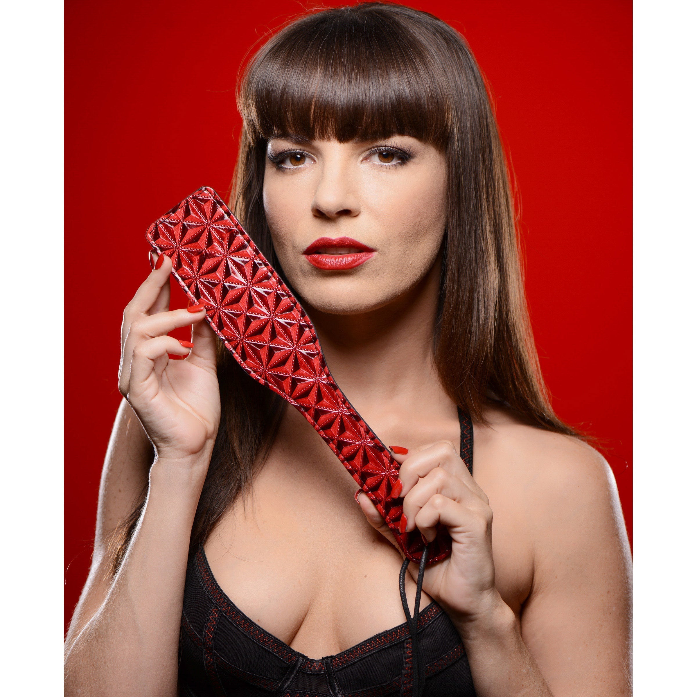 Woman in red attire holding the steel enforced spanking paddle