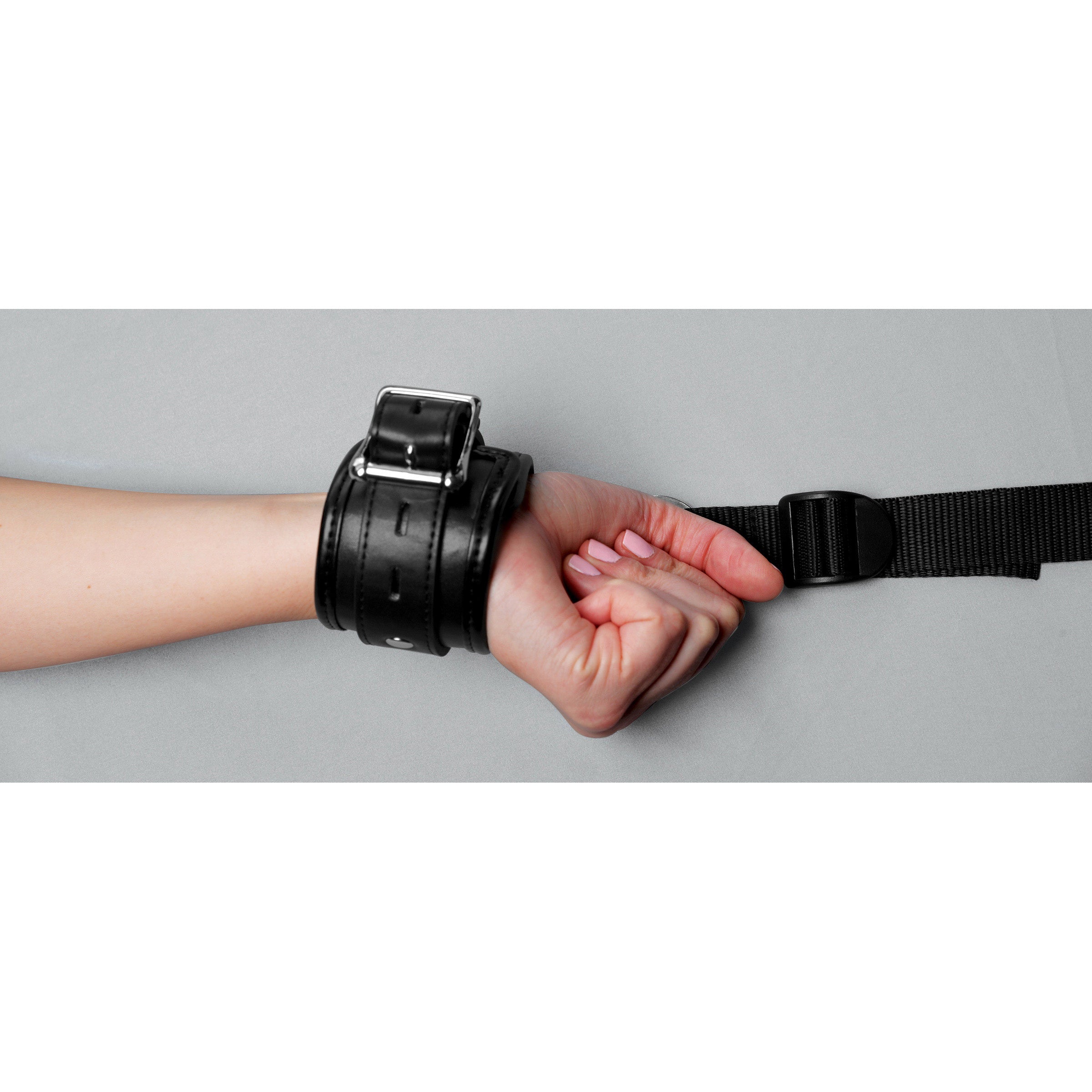 Close-up of a hand holding a black leather wrist cuff from the restraint kit