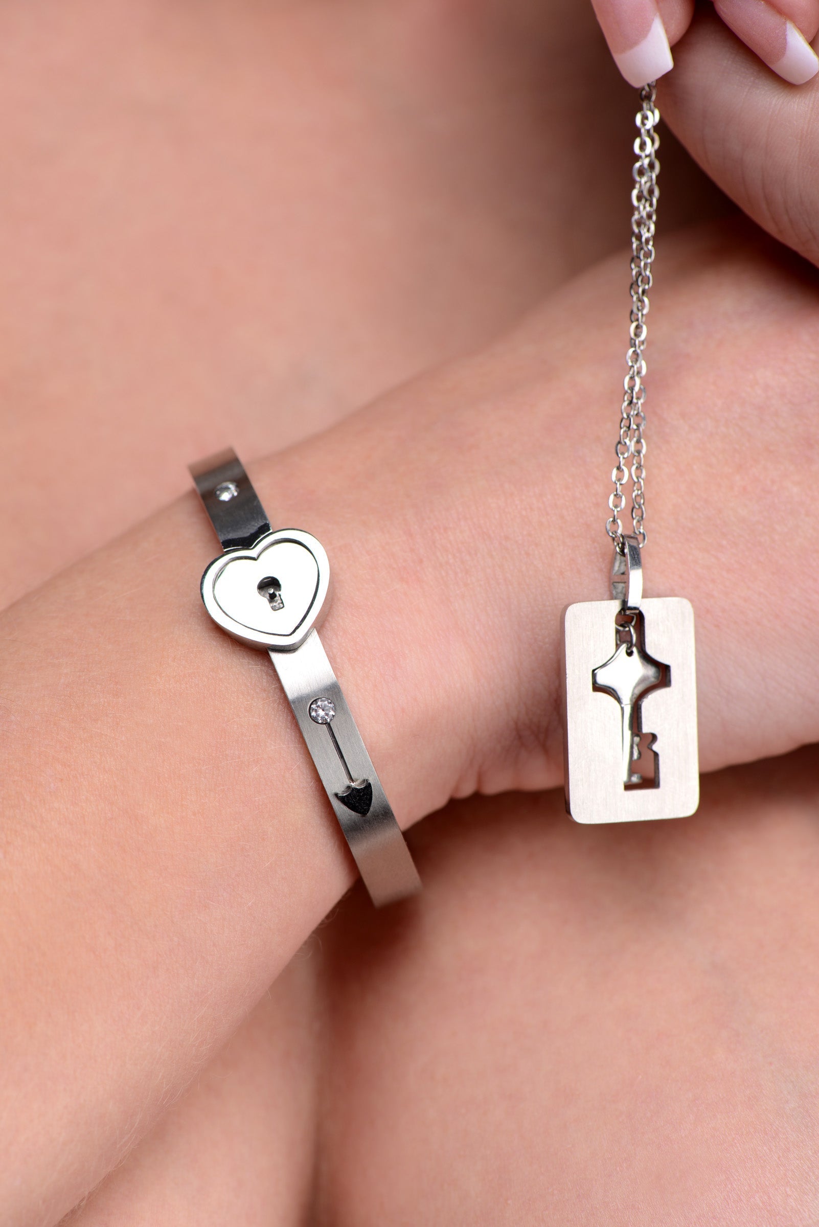 Female hand presenting a silver key designed to unlock a heart-shaped bracelet cuff